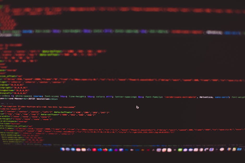 Close-up view of a computer screen displaying colorful lines of HTML code, with syntax highlighting in red, green, blue, and purple on a black background. The code includes various tags, attributes, a